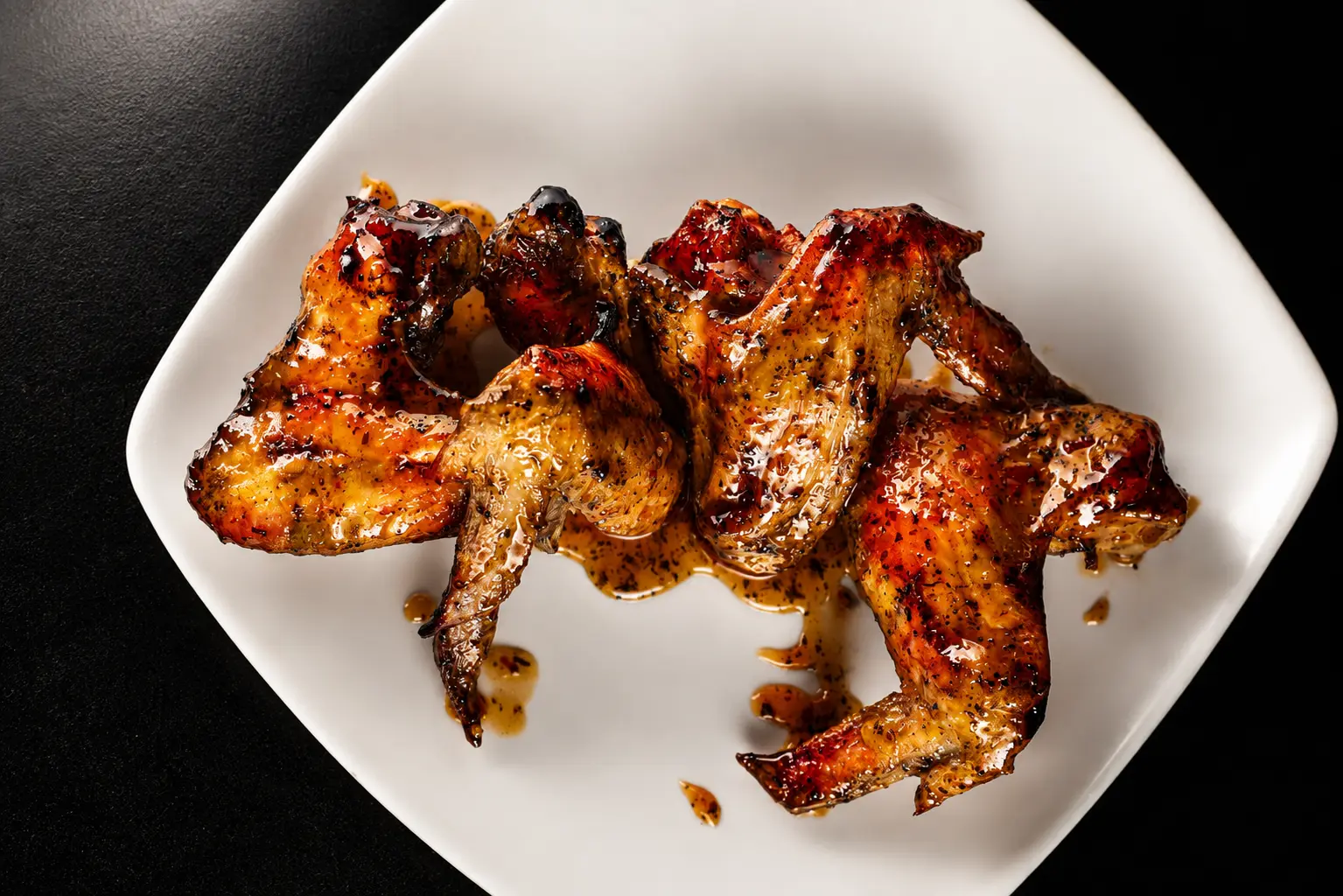 Four grilled jumbo chicken wings glazed in signature sauce on a white plate at The Block Bistro & Grill