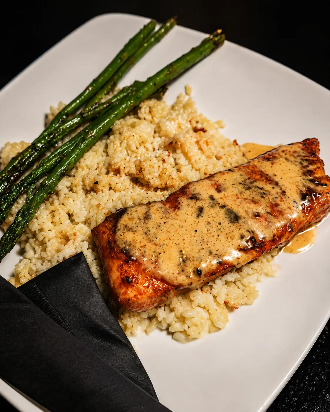 Blackened Cajun salmon with cream sauce over seasoned rice with grilled asparagus